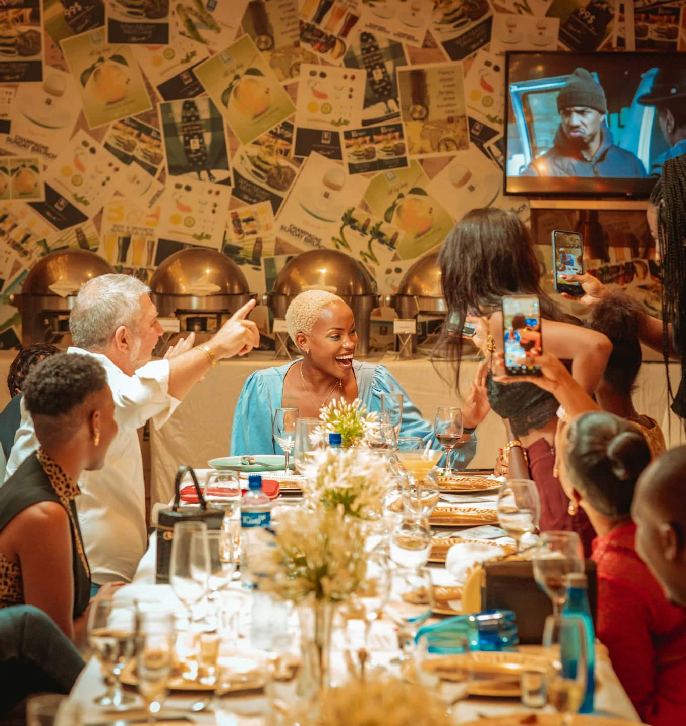 Persone ridono e scattano foto con smartphone attorno a un tavolo da pranzo.