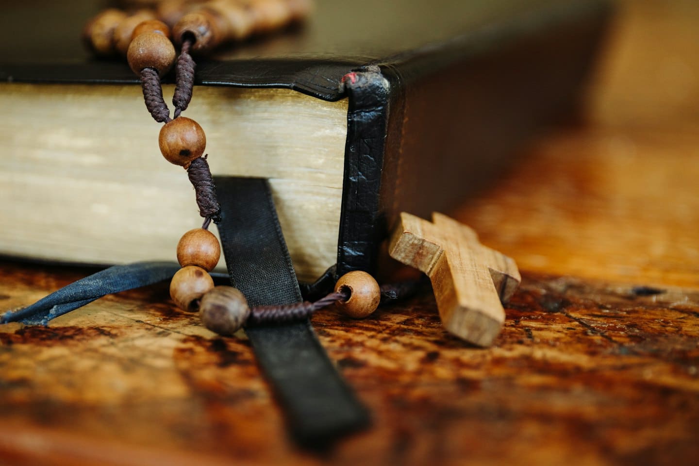 Una Bibbia nera con un rosario e una croce di legno.